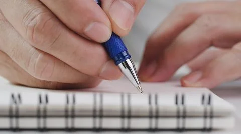 Close up hand writing paper on notebook with pen at office desk Stock Photos
