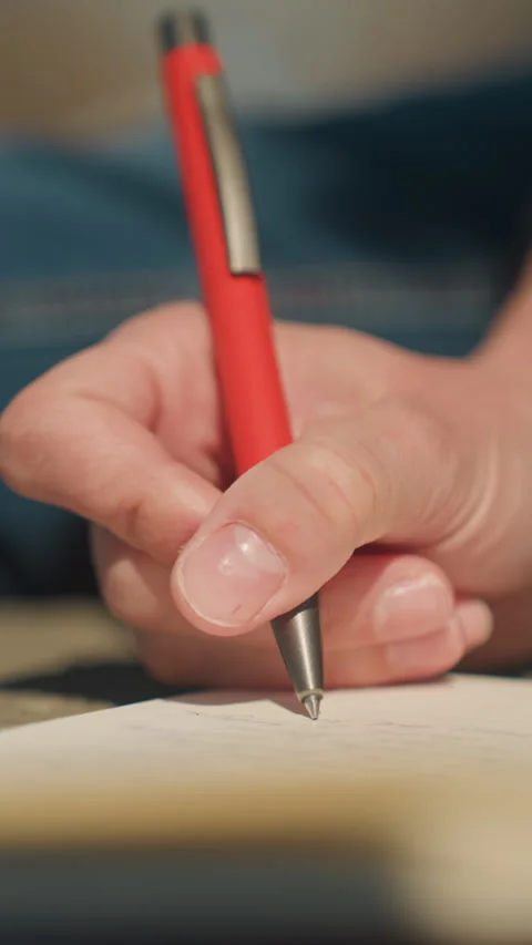 Close up hand writing on paper with red pen soft indoor natural lighting Stock Footage 345046528