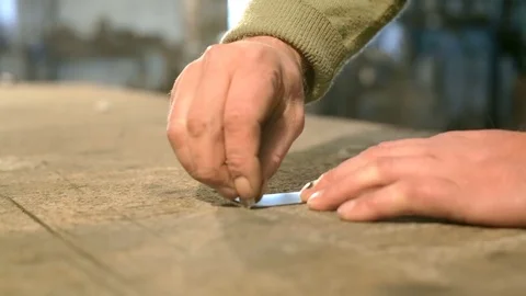 Close-up hand of a young blacksmith who draws a chalk line on the table with a Stock Footage 76410890