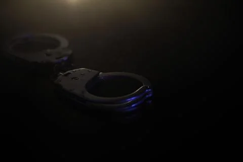Close-Up of Handcuffs in Dim Light with Shadow Play in Dark Background 스톡 사진