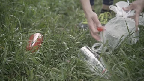 Close-up handheld shot of hands picking up plastic scattered on the grass Stock-Footage 242090715