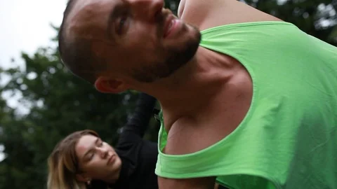 Close-up handheld shot of man and woman bending while exercising in park Video stock 120428745
