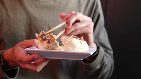Close up, handheld shot of man eating grilled rice ball with chopsticks Stock Footage 155776045