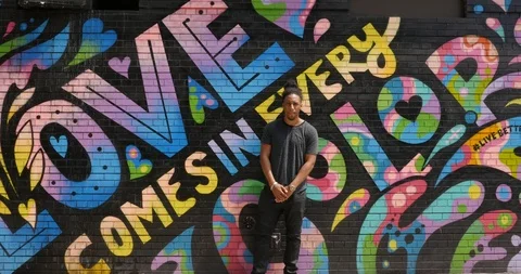 Close-up handheld shot of man posing near wall with colourful graffiti Stock Footage 120068983