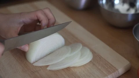 Close-up handheld shot of persons hand slicing white onion on chopping board Stock Footage 122481810