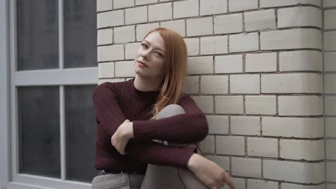 Close-up handheld shot of red haired young woman sitting against brick wall Stock Footage 114877916