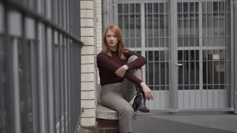 Close-up handheld shot of red haired young woman sitting on window sill Vídeos de archivo 114877922