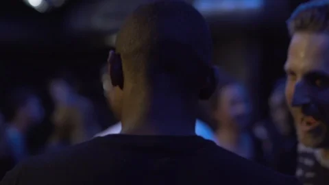 Close-up handheld shot of two young men talking and dancing in nightclub Stock Footage 114876421