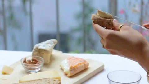 Close-up handheld shot of womans hand spreading cheese on bread 스톡 동영상 114867040