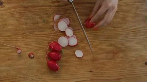Close-up handheld shot of womans hand chopping radishes on cutting board Stock Footage 114867165