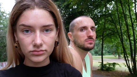 Close-up handheld shot of young couple in sportswear staring at camera in park Video stock 120430253