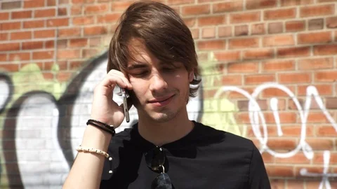 Close-up handheld shot of young man talking on smart phone against graffiti wall 스톡 동영상 114866395
