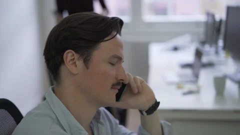 Close-up handheld shot of young man talking over the phone in office Stock Footage 114878035