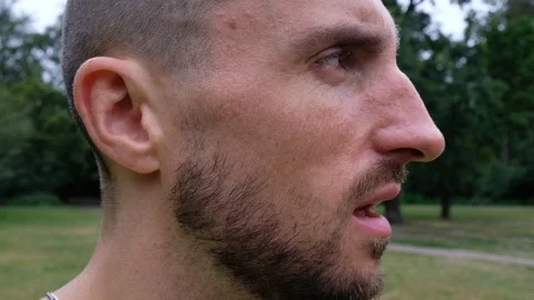 Close-up handheld shot of young man with beard breathing deeply in park Video stock 120428626