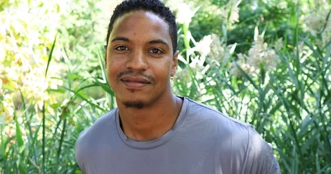 Close-up handheld shot of young man smiling at camera against grass Stock Footage 120432931
