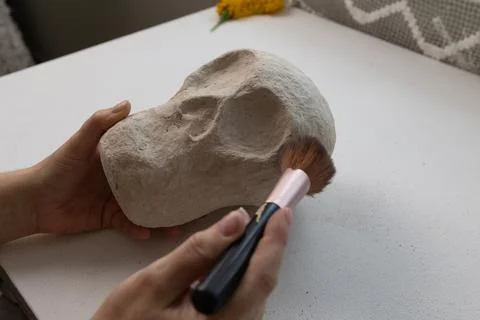 Close-up of a handmade plaster skull held in one hand, a brush smoothing a ro Stock Photos
