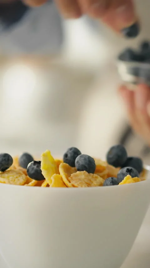 Close up of hands adding fresh berries to a healthy bowl of cereal flakes fo Stock Footage 331538323