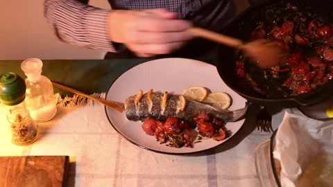 Close up of hands adding fresh tomato and olive salsa to baked fish on plate Vídeos de archivo 328255752