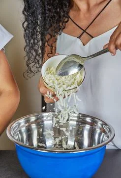 Close-up of hands adding grated cheese to a bowl, highlighting the cooking .. Stock Photos