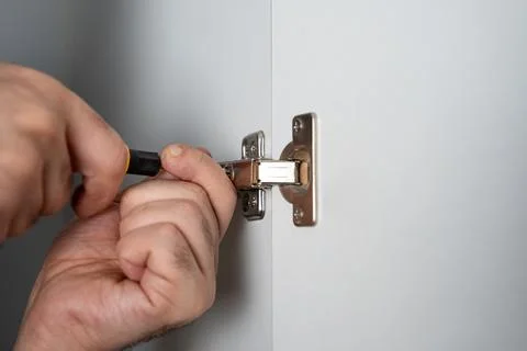 Close-up of hands adjusting a metal hinge on a wall using a screwdriver. Home Stock Photos