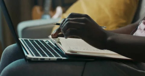 Close-up of hands of African-looking boy holding pencil and typing on laptop Stockbeeldmateriaal 218109706