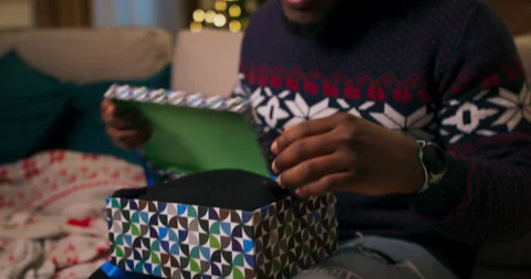 Close-up of the hands of African-looking guy who unpacks Christmas present. The 库存影片 211264620