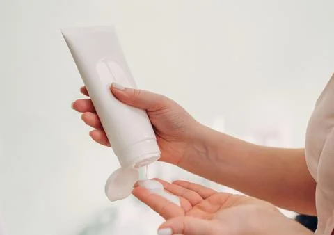 Close up of hands applying white moisturizer from tube, bodycare routine Stock Photos