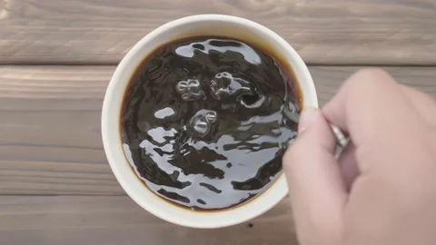 Close-up, hands are stirring hot coffee in a red-finished cup in 4K slow motion. Stock Footage 148737637