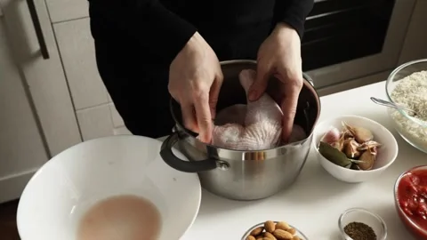 Close-up of hands arranging raw chicken pieces in a cooking pot beside garl.. 库存影片 334048500