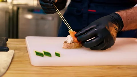 Close-up of hands in black gloves placing piece of salmon on bread with golden Stock Footage 273535585