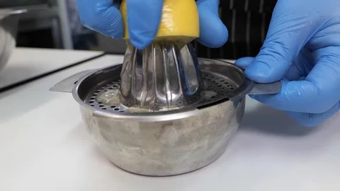 Close-up of hands in blue gloves manually juicing a fresh lemon with a stainless Stock Footage 331956671