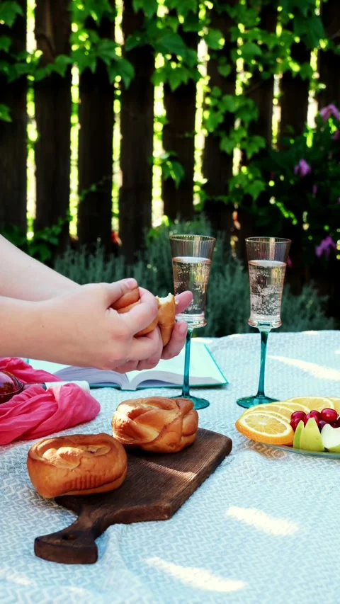 Close-up hands breaking braided rolls on wooden board during outdoor picnic in Stock Footage 345161994