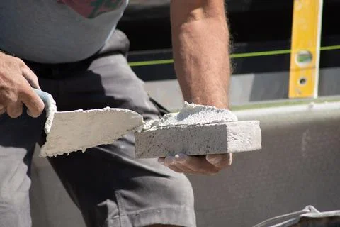 Close up of the hands of a bricklayer applying cement mortar to a brick Stock Photos