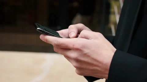 Close-up hands of a businessman typing a message on mobile phone outdoors at the Stock Footage 143354586