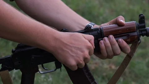Close-up of the hands of a camouflaged man loading bullets into a rifle chamber Stock Footage 125493197