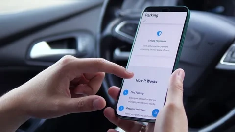 Close-up of hands in a car using a parking reservation app, displaying real-time Stock Footage 315029943