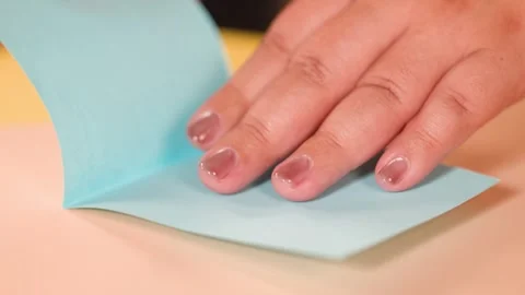 Close Up of Hands Carefully Folding Blue Origami Paper on Table Stock Footage 327120917