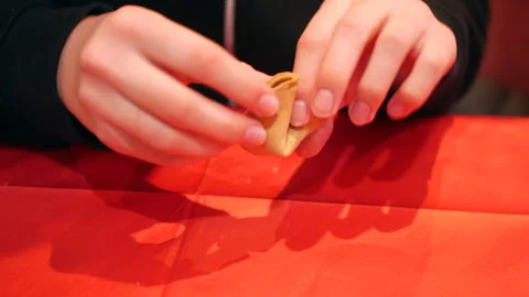 Close-up of hands carefully opening a fortune cookie on a bright red Stock Footage 283086943