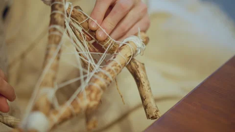 Close up of hands carefully tying white cord around wooden sticks to create Stock Footage 346735792