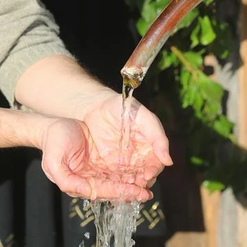 Close up hands catching fresh spring water from pipe Stock Photos