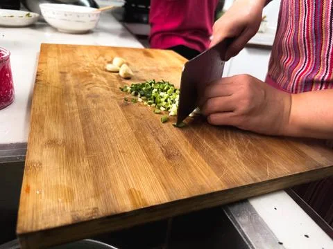 Close-up of hands chopping fresh spring onions on a wooden cutting board Foto stock