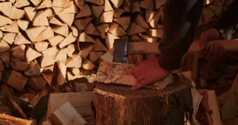 Close-up of hands chopping wood with an axe on a chopping block, with a woodpile Stock Footage 265010002
