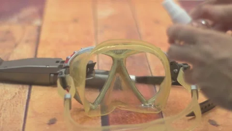 Close-up of hands cleaning a diving mask with anti-fog spray, prepping gear for Stock Footage 312671213