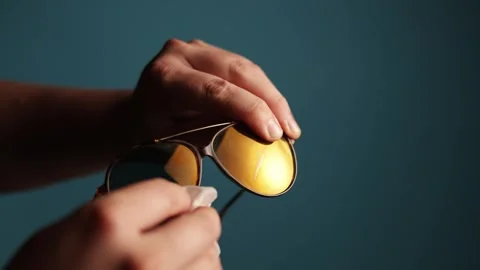 Close-up of hands cleaning yellow lens sunglasses with a white cloth Stock Footage 340266058