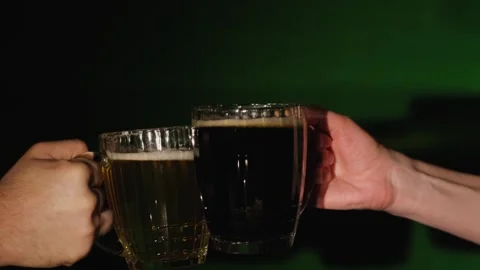 Close-up of hands clinking with beer mugs on a green background. Stock Footage 265771783
