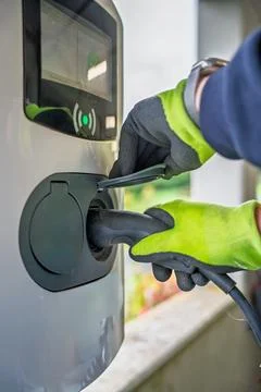 Close-up of hands connecting cables to an electric vehicle charger Stock Photos