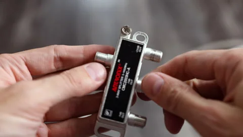 Close-up of hands connecting coaxial cables to a 3-way splitter, plugging OUT Stockbeeldmateriaal 312357955