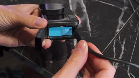 Close-up of hands connecting USB-C cable to action camera port, showing charging Stock Footage 333581285