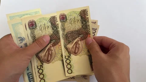 Close-up of hands counting Indonesian Rupiah of Different Years and Conditions Stock Footage 312587549