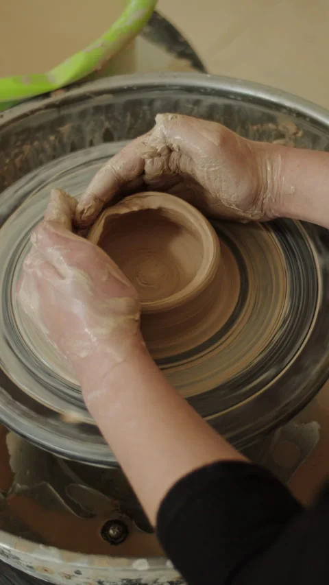 Close-up of hands covered in wet clay shaping a ceramic pot on a spinning Stock Footage 303514975